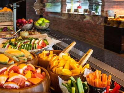 Buntes Buffet mit frischem Obst, Gemüse und Brötchen in rustikalen Holzschalen an Theke.