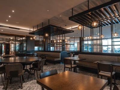 Moderner Gastraum mit dunklen Holztischen, Lederbänken und großen Fenstern, warme Beleuchtung.