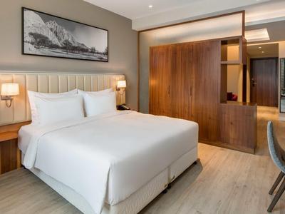 Modernes Schlafzimmer mit weißem Doppelbett, Holzmöbeln und minimalistischem Wandbild.