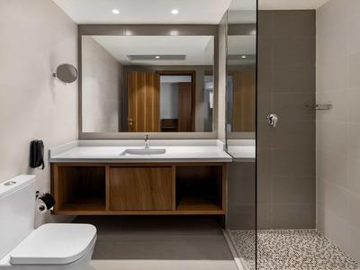 Helles modernes Badezimmer mit Glasdusche, großer Spiegelwand, Holzschrank und weißer Toilette.