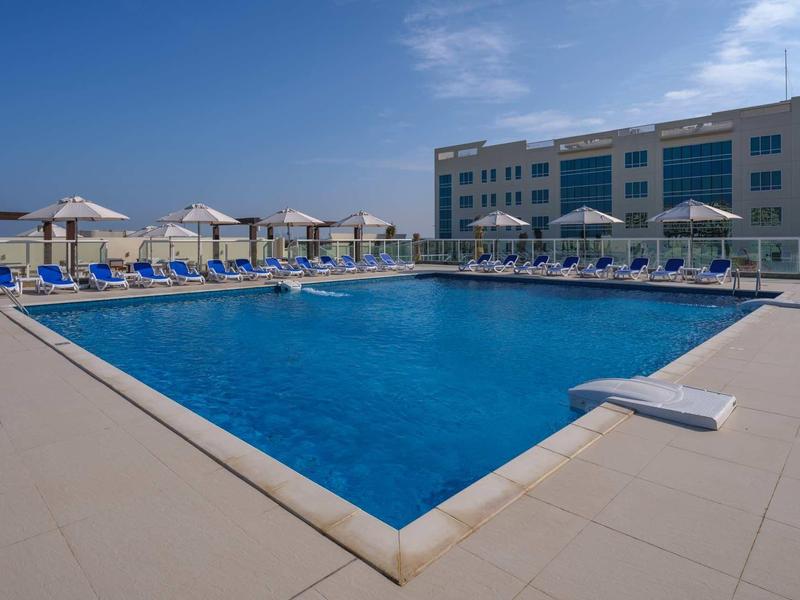 Großer rechteckiger Pool mit blauer Wasserfläche, umgeben von Liegestühlen und Sonnenschirmen.