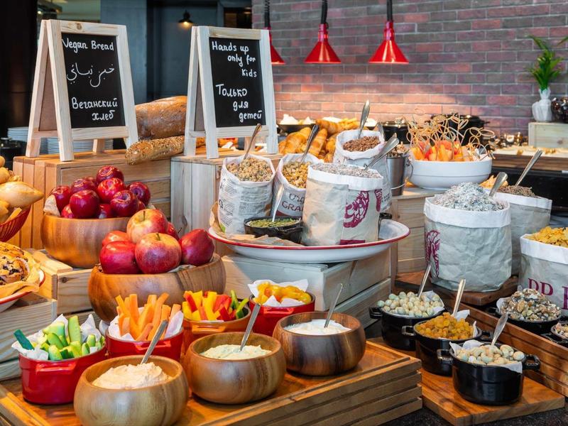 Buntes Buffet mit frischem Obst, Gebäck, Müsli und Körnern in Schalen und Körben auf Holztischen.