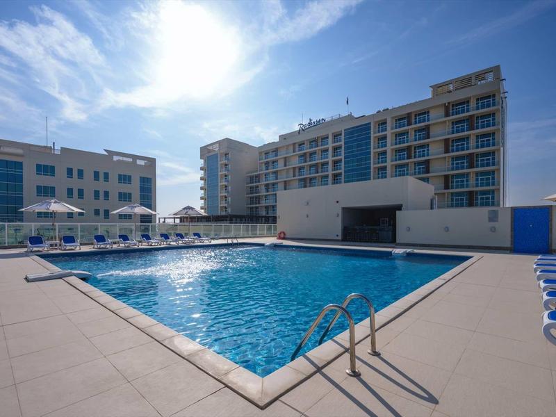 Moderner Außenpool mit klarem Wasser, umgeben von Liegestühlen und mehrstöckigen Gebäuden.