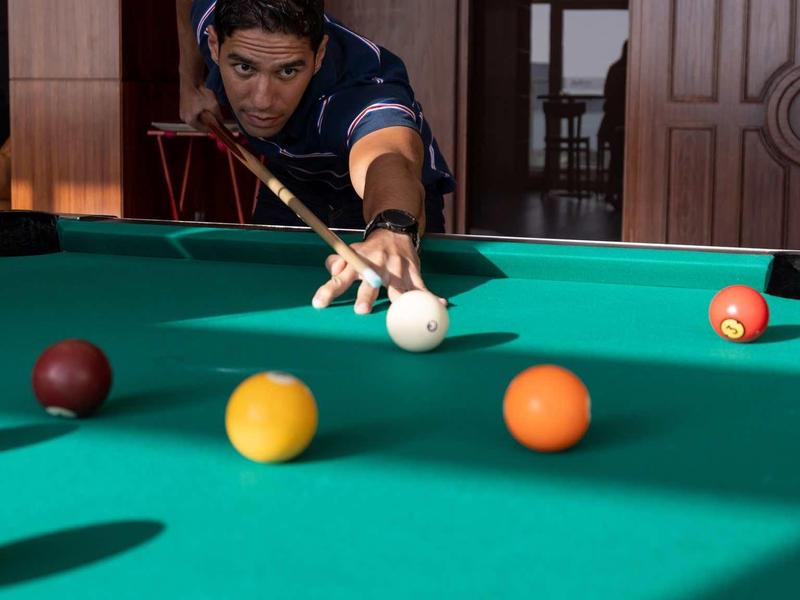 Mann spielt Billiard, konzentriert zielt mit Queue auf weißen Kugel am grünen Tisch in Holzraum.