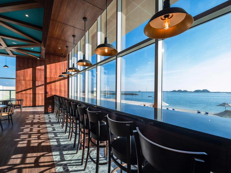 Moderne Bar mit schwarzen Hockern und großen Fenstern, Blick auf das blaue Meer und Inseln.