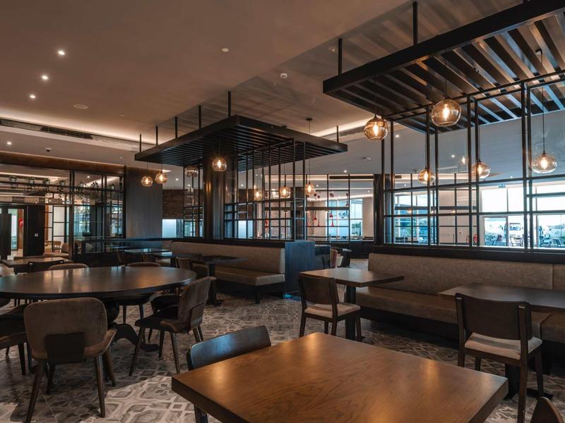 Moderner Gastraum mit dunklen Holztischen, Lederbänken und großen Fenstern, warme Beleuchtung.