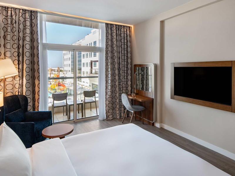 Modernes Hotelzimmer mit großem Bett, Sofa, Schreibtisch und Balkon mit Stadtblick.