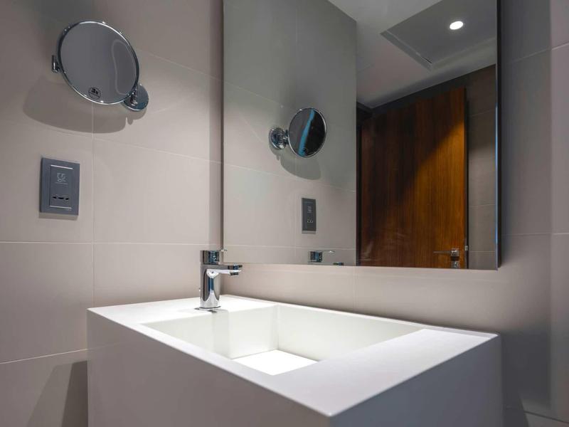 Moderner Badezimmerspiegel mit eckigem weißen Waschbecken und kleinem rundem Vergrößerungsspiegel.