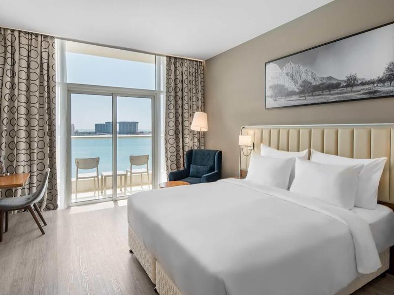 Modernes Hotelzimmer mit großem Bett, Balkon mit Meerblick und stilvoller Einrichtung.