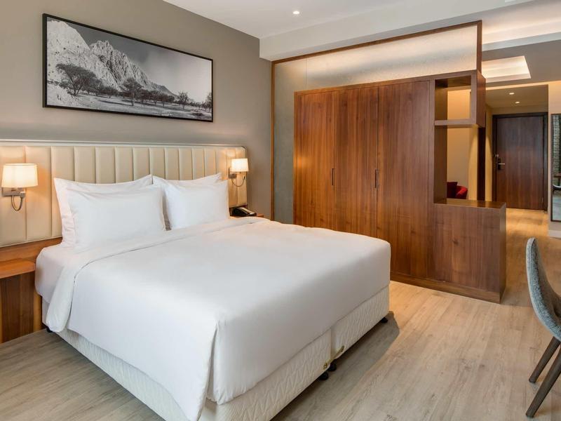 Modernes Schlafzimmer mit weißem Doppelbett, Holzmöbeln und minimalistischem Wandbild.