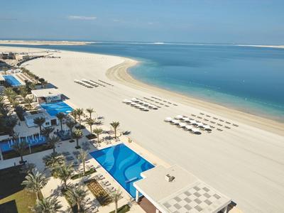 Strand mit Reihen von Liegestühlen, blauem Pool, Palmen und klarem, ruhigem Meer unter blauem Himmel.