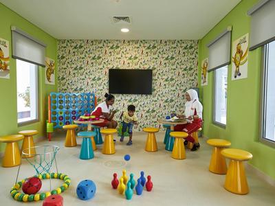 Kinderspielzimmer mit bunten Hockern, Spielzeugkegeln und grünen Wänden, zwei Kinder und Erwachsene.