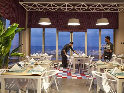 Moderner Restaurantraum mit weißen Stühlen, gedeckten Tischen und großen Fenstern mit Meerblick.