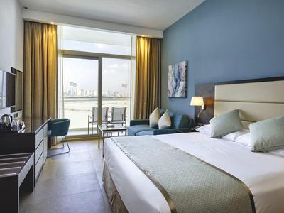 Modernes Hotelzimmer mit großem Bett, blauer Wand, TV, Sesseln und Balkon mit Stadtblick.