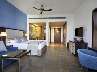 Modernes Hotelzimmer mit großem Bett, blauen Akzenten, Fliesenboden und Glasdusche im Hintergrund.