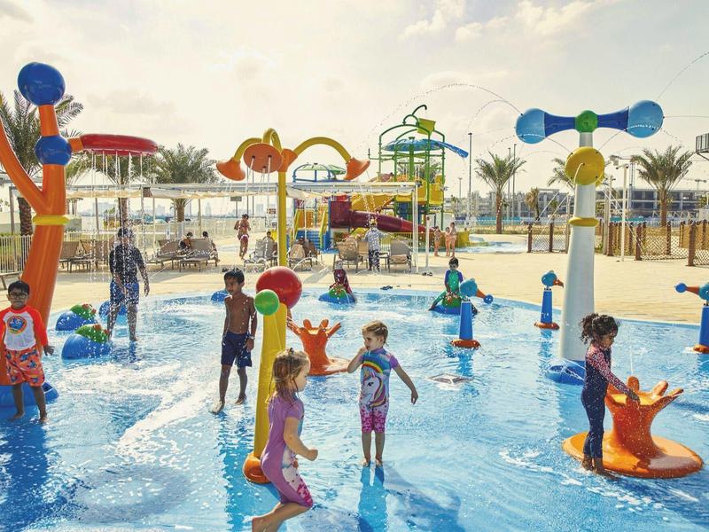 Children playing in colorful water park with water features and slippery attractions.