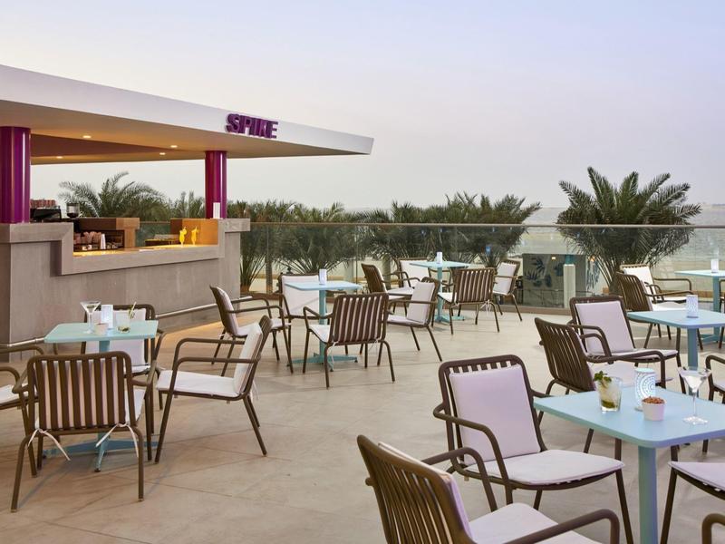 Open terrace with tables, chairs, and bar overlooking palm trees at sunset.