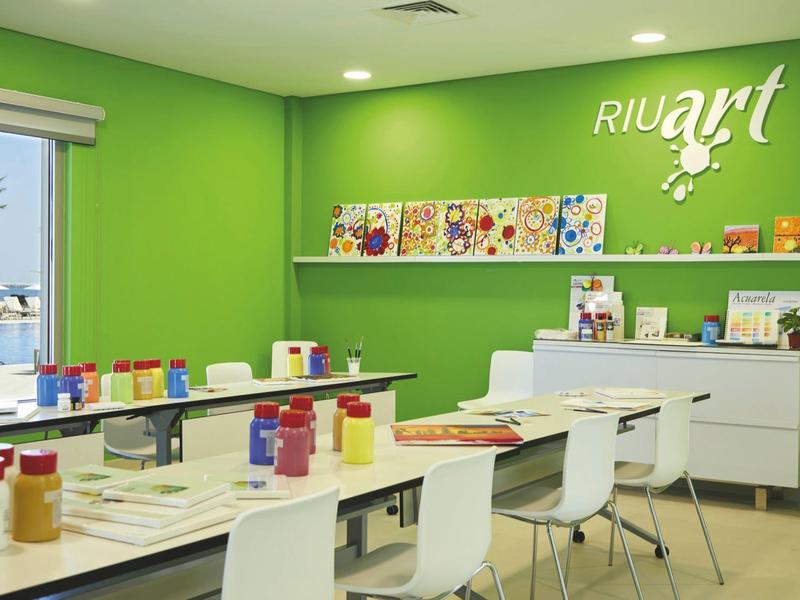 Bright green room with tables and white chairs, colorful paint containers on top.