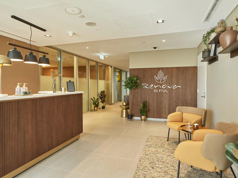 Modern hotel lobby with reception desk, seating area, and plants in warm tones.