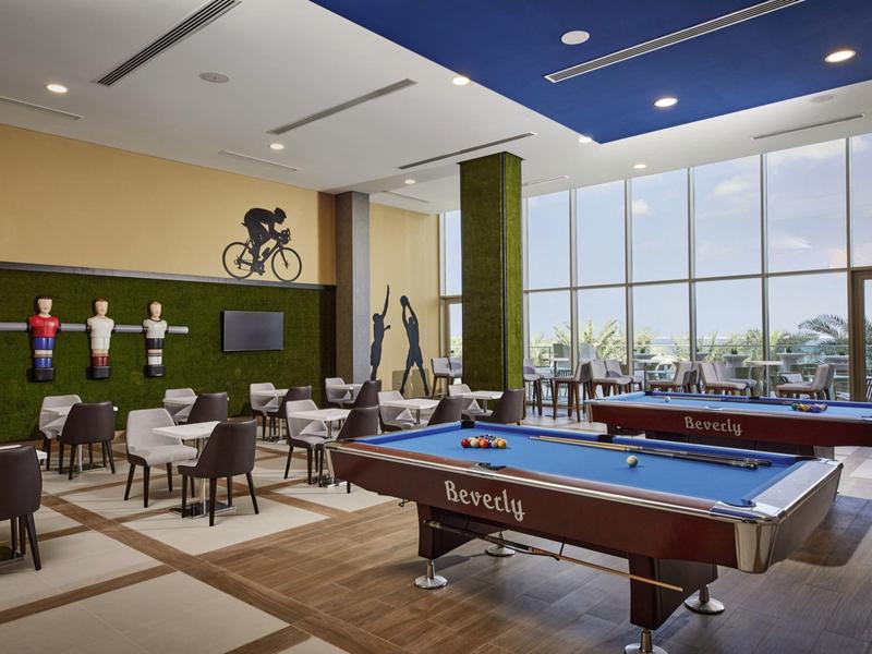 Modern game room with pool tables, foosball table, seating, and large windows with a view.