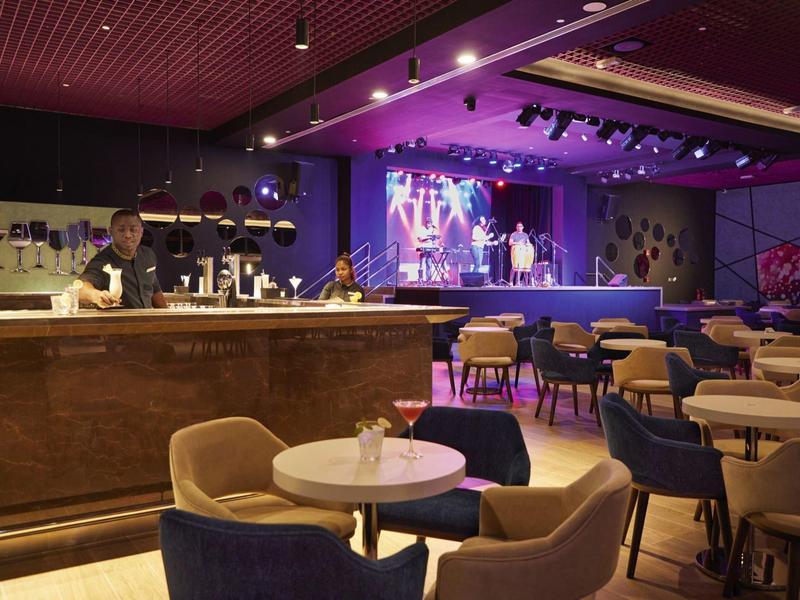 Empty lounge area with tables, chairs, and a lit stage in an elegant setting.