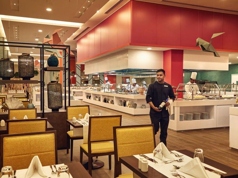 Modern restaurant with yellow chairs, set tables, and serving staff.