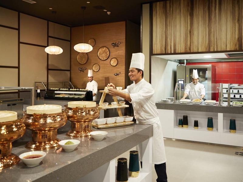 Chef in white outfit preparing food in modern hotel kitchen.