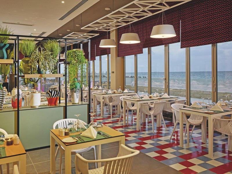 Bright restaurant with sea view, colorful floor, and modern wooden furniture.