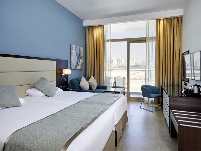 Modern hotel room with double bed, blue accent wall, and large curtains on window.
