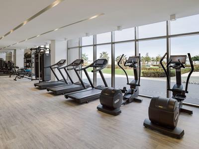 Helle Fitnessstudio mit Laufbändern und Ellipsentrainern vor großen Fenstern mit Ausblick.
