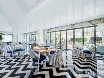 Modernes Restaurant mit großen Fenstern, Teppich mit Zickzack-Muster und gepolsterten Stühlen.