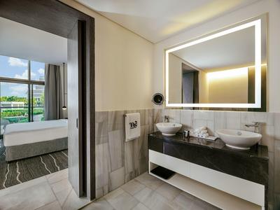 Modernes Badezimmer mit beleuchtetem Spiegel, zwei Waschbecken und Blick ins Schlafzimmer.