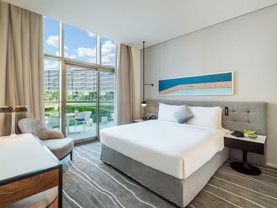 Helles Schlafzimmer mit großem Bett, Teppichboden, Schreibtisch und Balkon mit Blick ins Grüne.