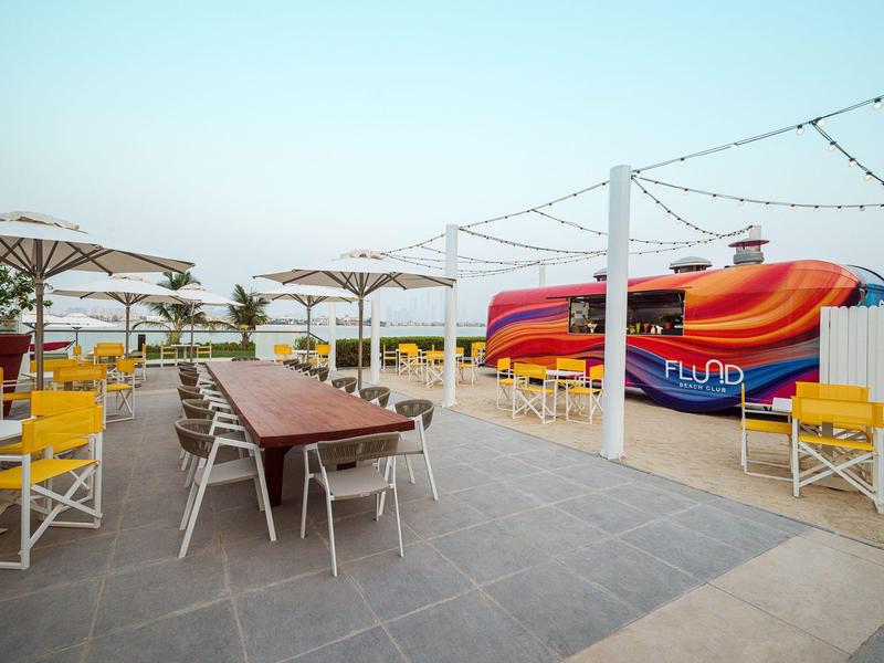 Outdoor-Sitzbereich mit gelben Stühlen, Tischen und buntem Hüpfkissen im Hintergrund.