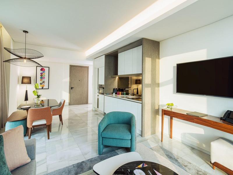 Moderner Wohnraum mit offener Küche, blauer Sessel, Esstisch mit Stühlen und Wand-TV.