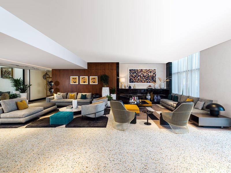 Großer Wohnraum mit modernen Sofas, Sesseln, Teppichen und Kunstwerken an weißen Wänden.