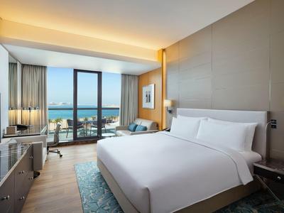 Modernes Hotelzimmer mit großem Bett, großen Fenstern und Meerblick bei Tageslicht.