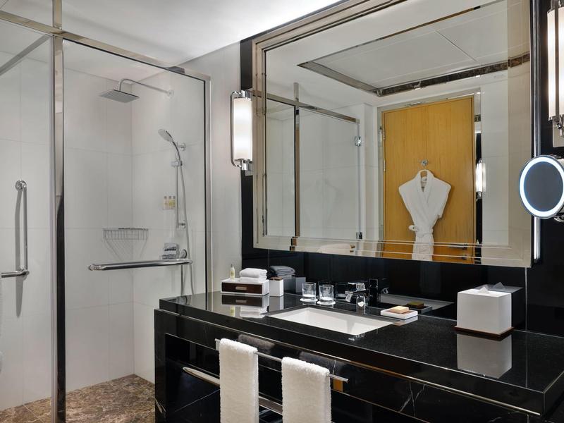 Elegantes Hotelbadezimmer mit schwarzer Marmorarbeitsplatte, großer Spiegel und Glasdusche.