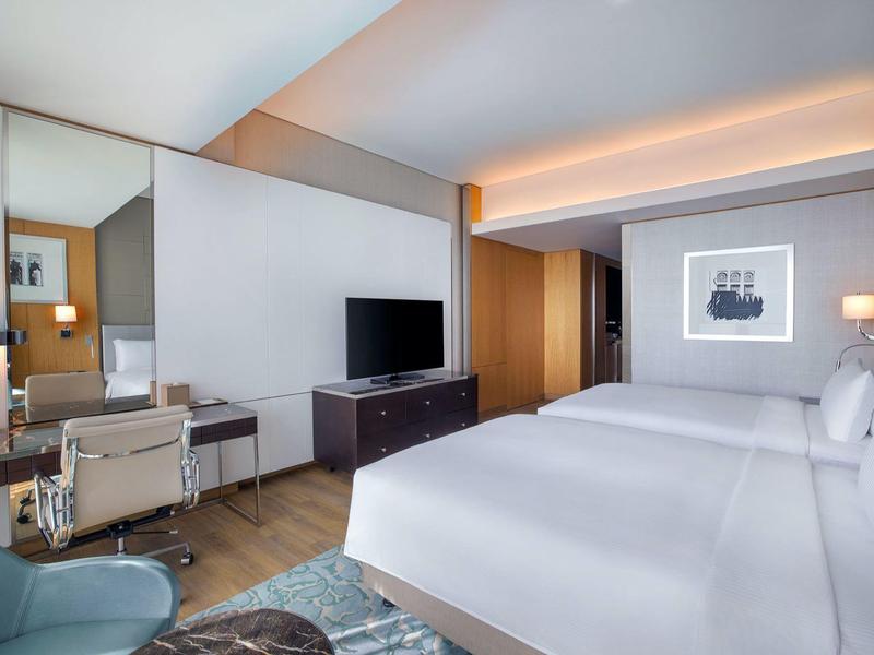 Modernes Hotelzimmer mit zwei Doppelbetten, Schreibtisch, Fernseher und neutralen Farbtönen.