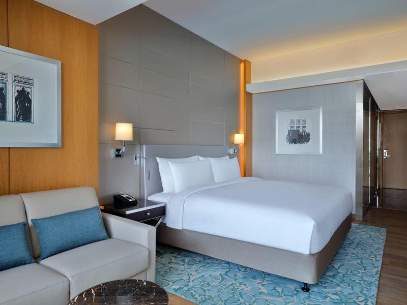 Modernes Hotelzimmer mit großem Bett, Sofa, Teppich und attraktiver Beleuchtung.