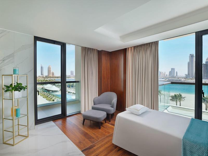 Modernes Hotelzimmer mit Liege, großen Fenstern und Blick auf Wasser und Stadt.