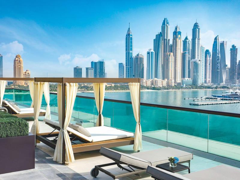 Luxuriöse Terrasse mit Himmelbetten und Blick auf moderne Wolkenkratzer an der Küste.