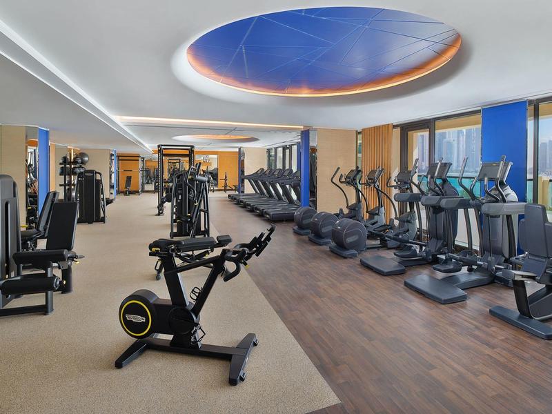 Moderner Fitnessraum mit Trainingsgeräten, Laufbändern und großem rundem Deckenfenster mit Blick zum Himmel.