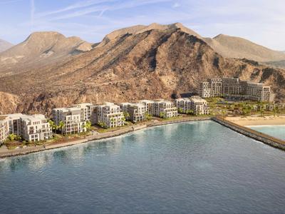 Küstenhotelanlage mit Bergen im Hintergrund und Hafenmole im Vordergrund.