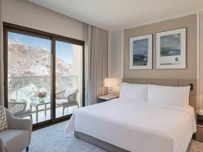 Helles Schlafzimmer mit großem Bett, Sessel, zwei Bildern an der Wand und Balkon mit Bergblick.