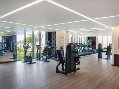 Heller, moderner Fitnessraum mit Cardiogeräten und Gewichten und großen Fenstern mit Blick ins Freie.
