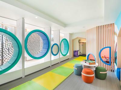 Bunten Kinderspielraum mit Netzwänden, Sitzhockern und farbigen Matten in einem hellen Raum.