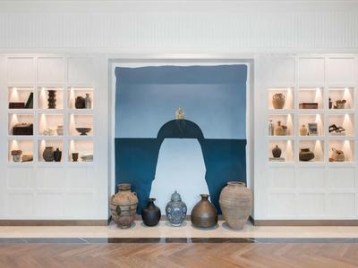 Museumsausstellung mit antiken Tongefäßen, weißen Wänden und großem blauen Wandbild im Hintergrund.