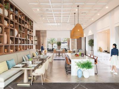 Heller, moderner Speisesaal mit Holzmöbeln, Pflanzen und Gästen in entspannter Atmosphäre.