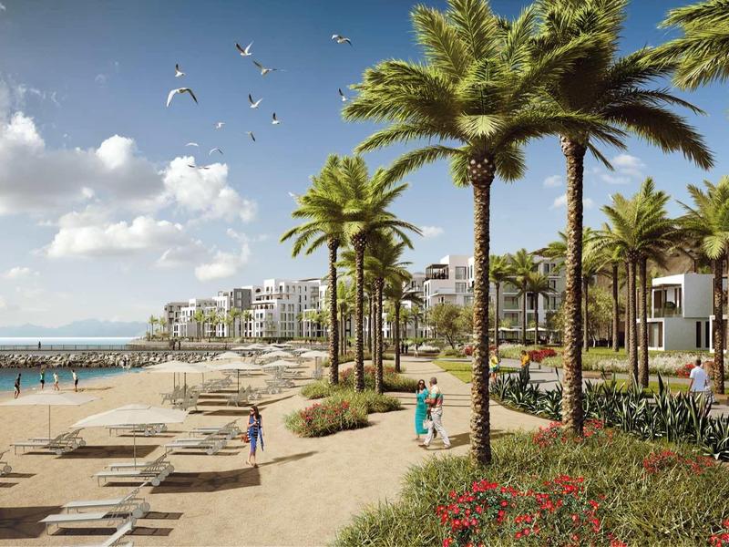 Strand mit Palmen, Liegestühlen und moderner Strandpromenade unter blauem Himmel.